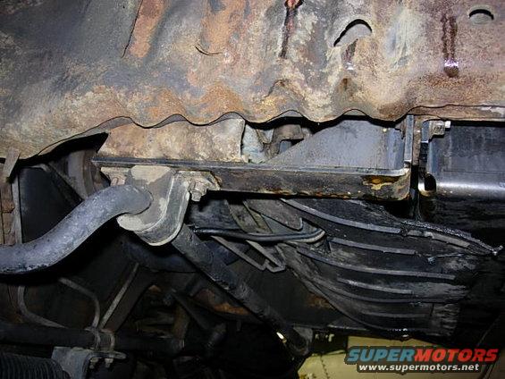 Underside view of a rusty vehicle frame with suspension parts and wiring visible
