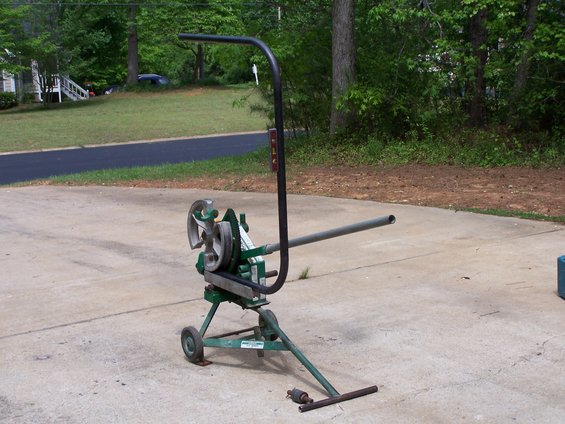 Green pipe bender with a long metal pipe attached, on a concrete driveway