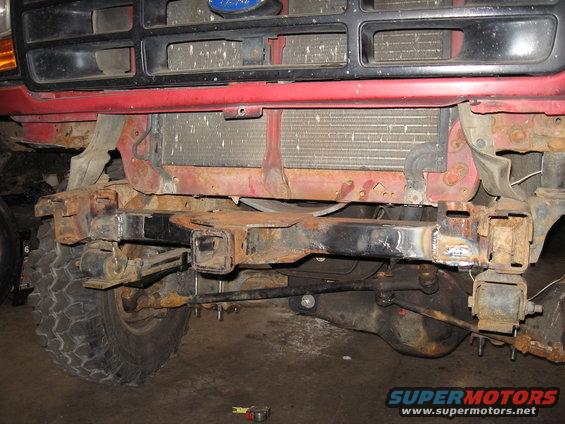 Front end of a rusty Ford truck, showing the grille, radiator, and frame