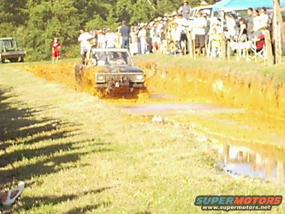 Mud-splattered 1978 Ford Bronco driving through a mud pit with spectators in the background