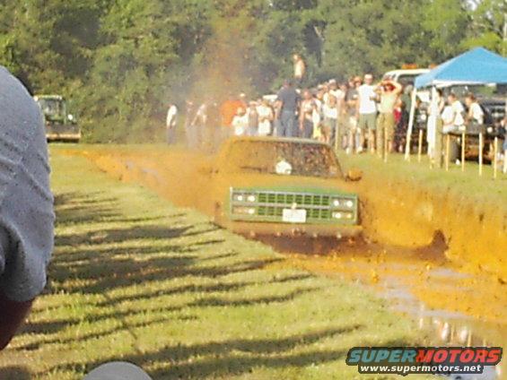 Green pickup truck stuck in mud, front view. Grille and headlights visible