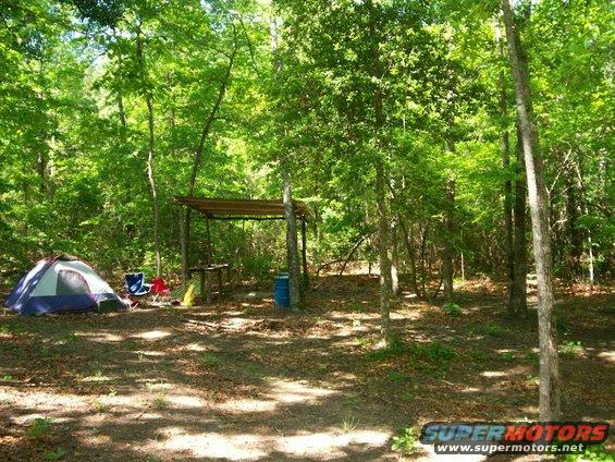 Campsite with a tent, chairs, and a covered shelter in a wooded area
