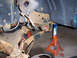 1996 Ford Bronco - A person works on the rusty suspension of a vehicle supported by jack stands.