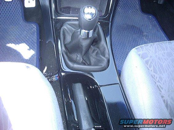 Car interior showing a manual gear shifter, handbrake, and blue floor mats