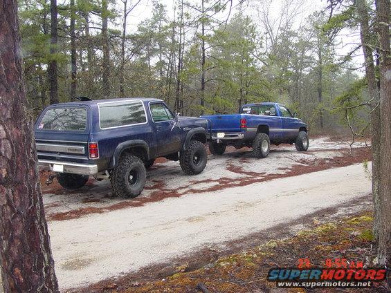 Two blue pickup trucks with lifted suspensions on a dirt road