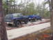 1995 Dodge 1500 - Two lifted blue pickup trucks are seen on a dirt road in a wooded area, with one truck towing a trailer.