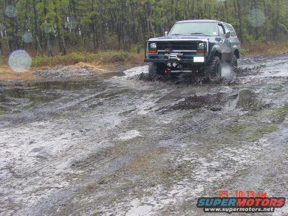 Blue Dodge Ramcharger driving through a muddy trail with trees in the background