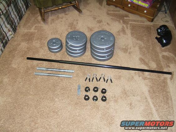Weight plates, barbell, and collars laid out on a carpeted floor