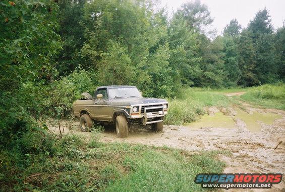 Muddy 1978 Ford F-Series pickup truck driving on a dirt track with puddles