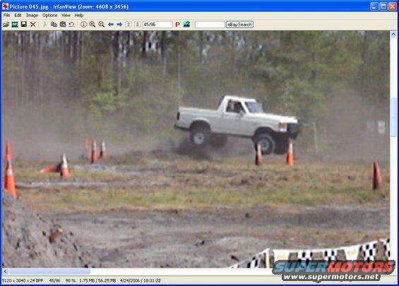 White pickup truck jumping over dirt track with orange cones