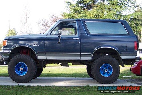 Blue Ford Bronco with lifted suspension and bright blue wheels parked on a driveway