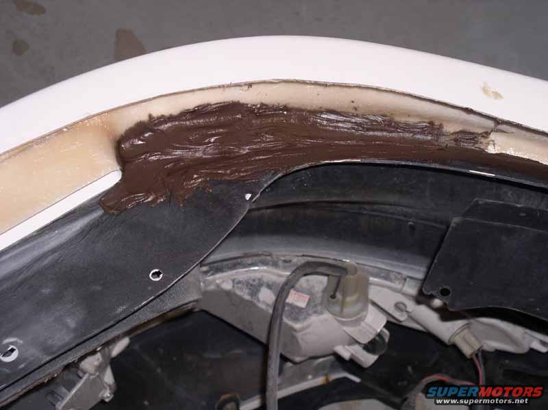 close-up of brown putty being applied to a car's fender seam