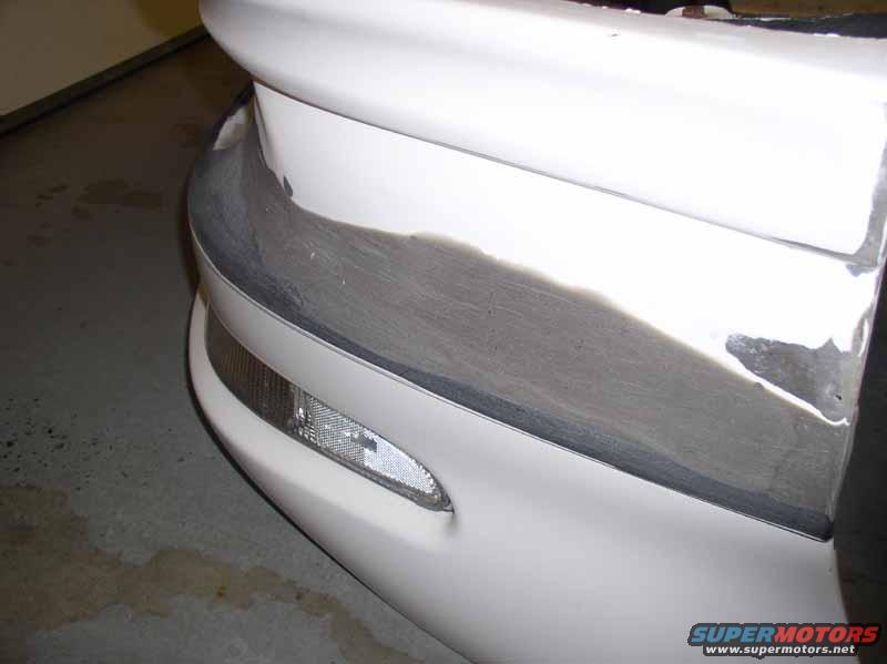 Close-up of a car's front bumper undergoing repair, showing primer and body filler