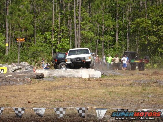 White pickup truck with a black SUV behind it, driving on an obstacle course