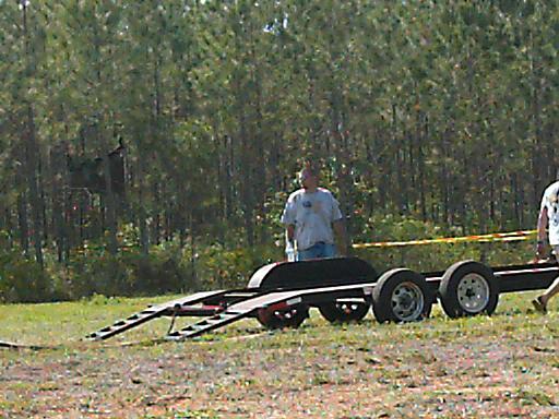 Car trailer with two people standing nearby, trees in background