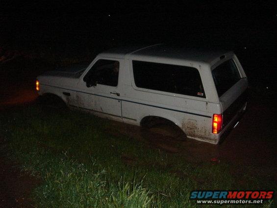 White Ford Bronco stuck in mud at night, side view. Mud covers the lower body and tires
