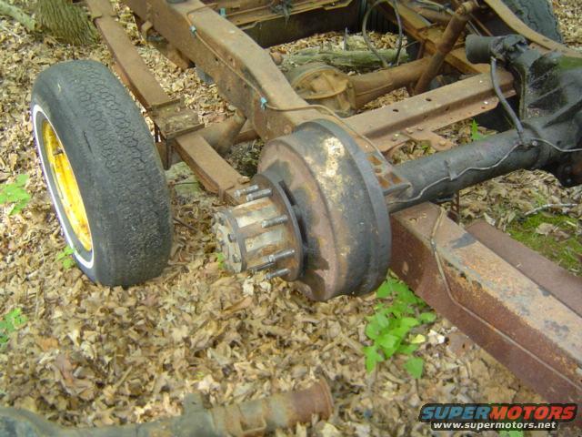 rusty truck frame showing rear axle, leaf springs, and a wheel with a white sidewall