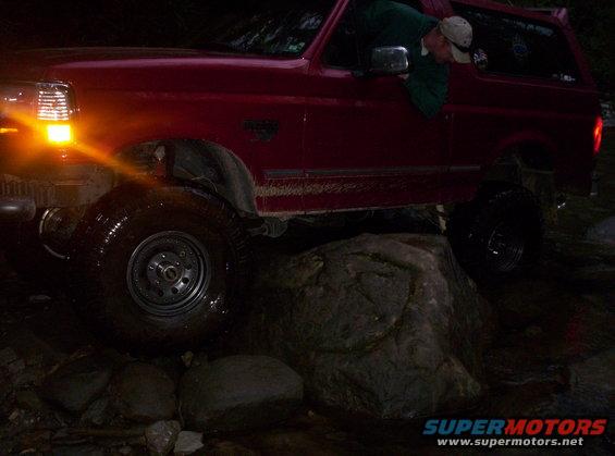 1995 Ford Bronco driving over large rocks at night, front wheel turned