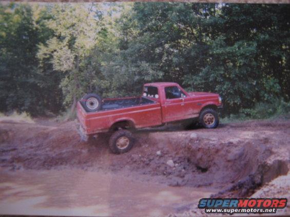 Red pickup truck with a spare tire in the bed, driving off-road on a muddy incline
