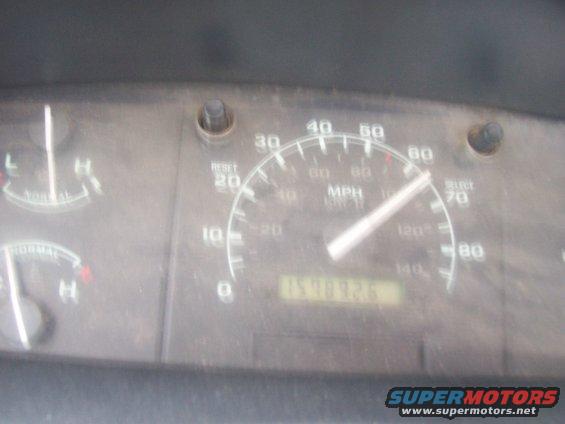 Close-up of a dusty dashboard with a speedometer, fuel gauge, and odometer showing 154832.6 miles