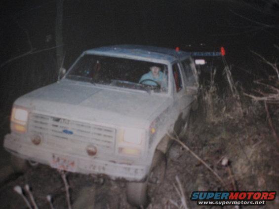 White Ford Bronco II stuck in mud at night, driver visible