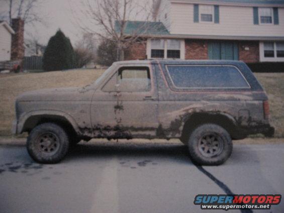 Side view of a dirty, second-generation Ford Bronco parked on a street