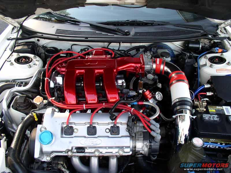Engine bay with shiny red intake manifold and Ford branding on silver engine block