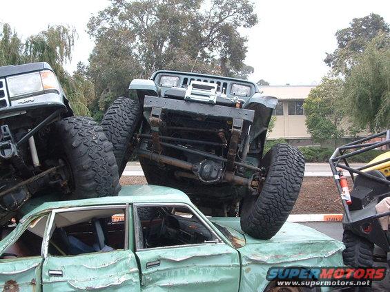 Green 1994 Jeep YJ on top of a crushed sedan, front view