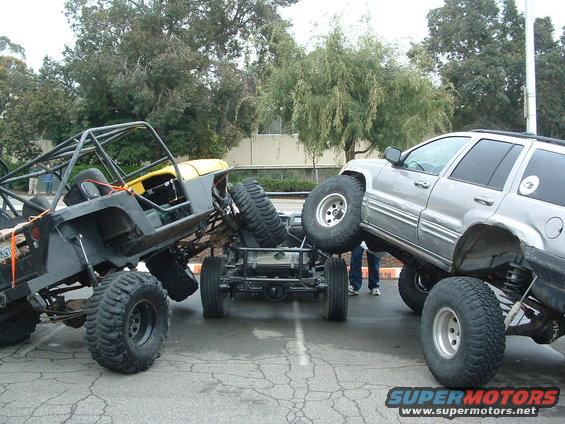 Modified Jeep YJ and silver SUV with large tires, one vehicle on top of the other