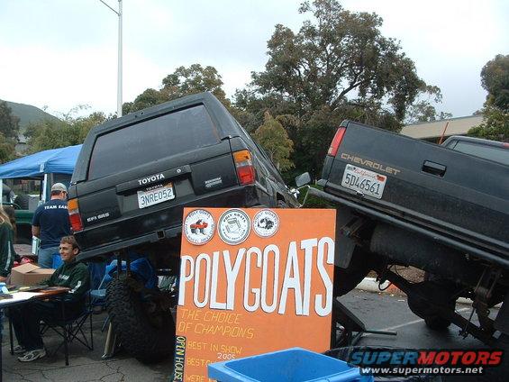 Rear view of black Toyota 4Runner lifted on Chevrolet truck, with 'POLYCOATS' sign