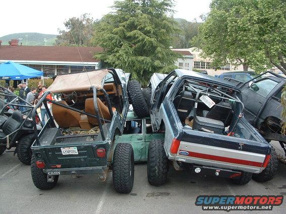 Several off-road vehicles, including a green Jeep YJ and a blue pickup, are tightly packed together in a parking lot