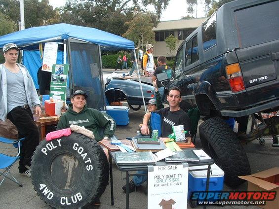 Lifted black SUV with large tires, people at a table with a tire that says POLY GOATS 4WD CLUB