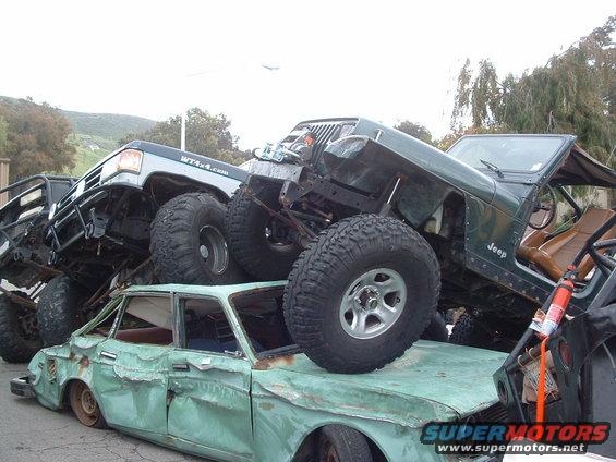 Three wrecked off-road vehicles piled on top of a crushed sedan. One Jeep is visible