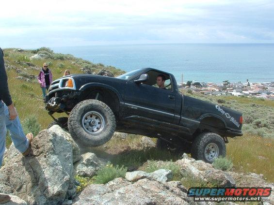 Black pickup truck with lifted suspension navigating rocky terrain