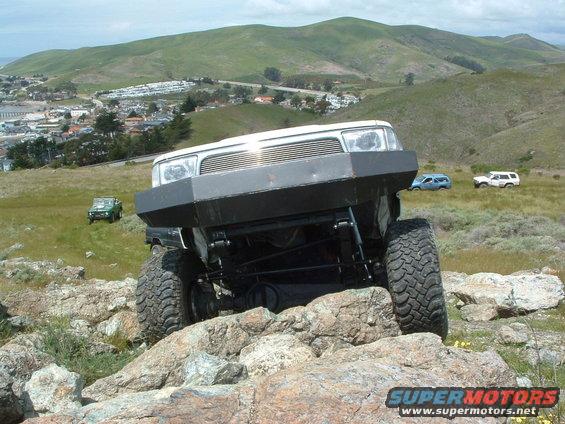 White off-road vehicle with custom bumper on rocks, front view. Other vehicles visible in background