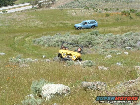 Yellow Jeep CJ-7 and blue SUV driving off-road on a grassy hill