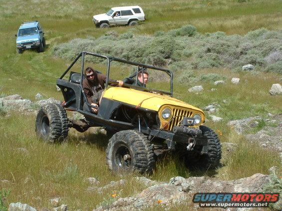 Yellow custom buggy with roll cage and large tires, driven off-road with two people inside