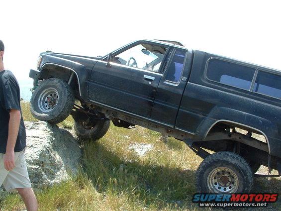 Black pickup truck with camper shell climbing a rock