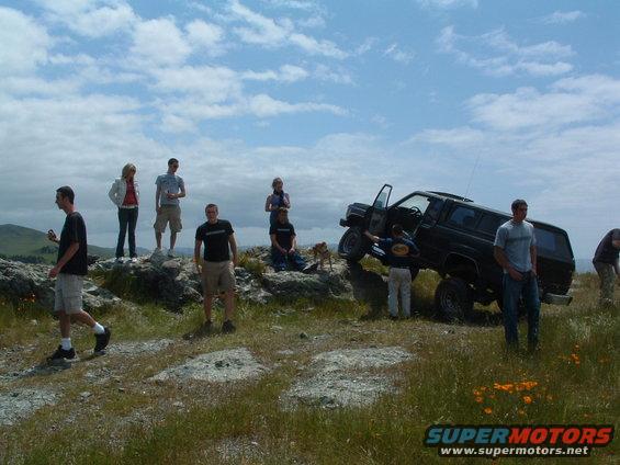 Black SUV with doors open parked on a rocky incline, several people standing around