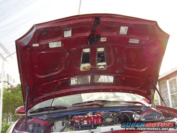 Car hood open showing engine and underside of hood with stickers