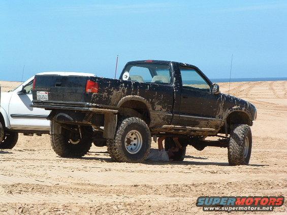 Black lifted pickup truck on sand, with a white vehicle beside it