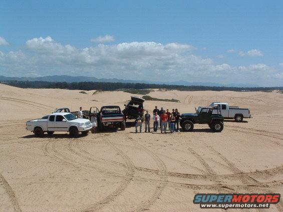 Group of people standing with several off-road vehicles in a sandy, dune-filled landscape