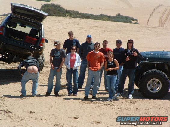 Green Jeep Wrangler with a group of people and an open-trunk SUV in sand dunes