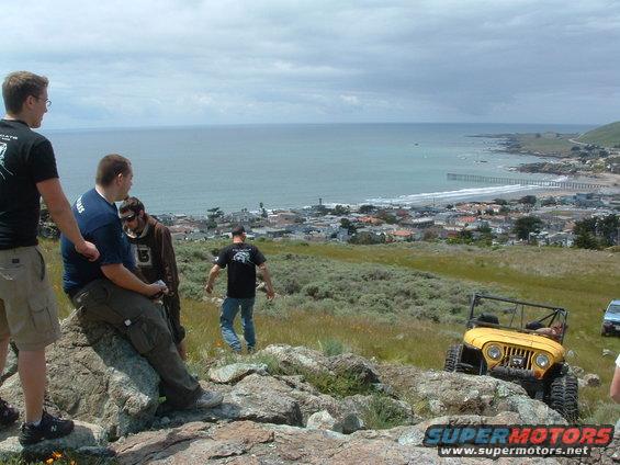 Yellow Jeep CJ-7 on rocky terrain with coastal town in background