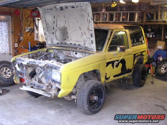 Yellow SUV with hood open, showing engine bay. Black peeling paint on doors