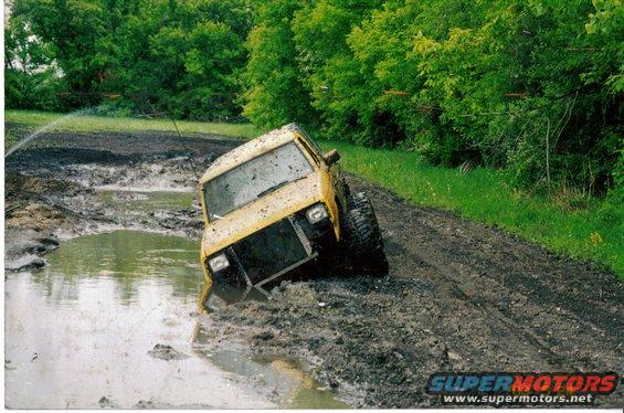 Yellow off-road vehicle stuck in mud, front grille removed, tires large