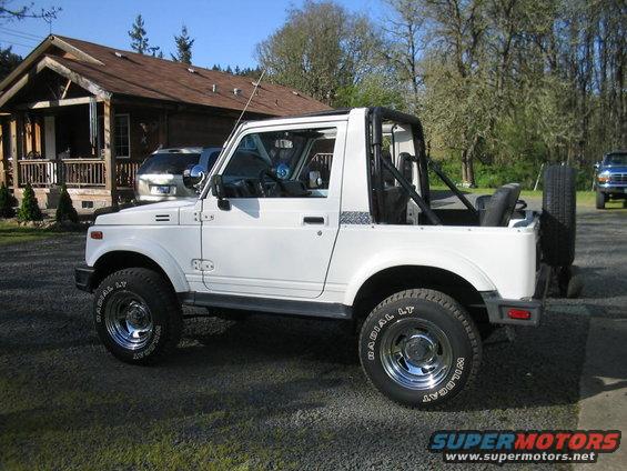 1987 Suzuki Samurai, white, parked in gravel driveway with a house and trees in background. Another vehicle is parked in front of the house