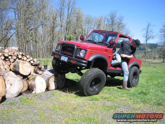 1987 Suzuki Samurai with lifted suspension and large tires climbing over a pile of logs