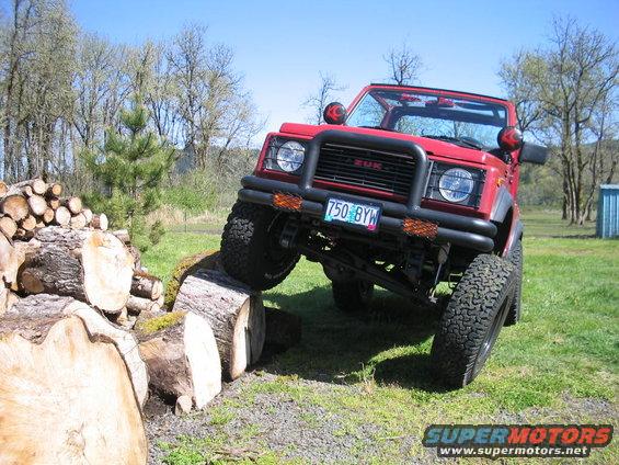 Red Suzuki Samurai climbing over logs. License plate reads 750 BYW