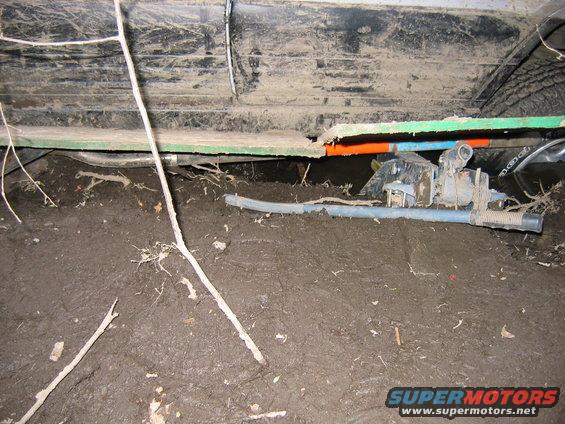 Undercarriage of a vehicle stuck in mud, showing suspension and exhaust components